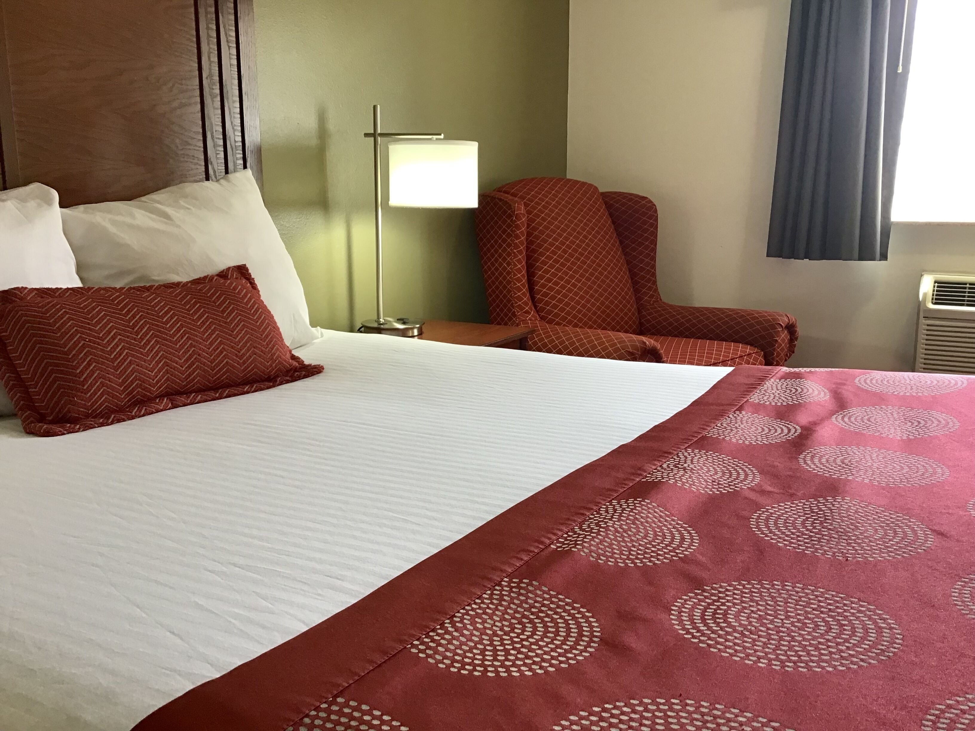 Ein Hotelzimmer mit Bett, Stuhl, Lampe und einem Fenster mit Vorhängen.