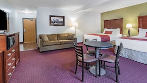 A hotel room with a bed, a sofa, a dining table with chairs, a TV, and a lamp. - Baymont by Wyndham Bozeman (Bozeman)