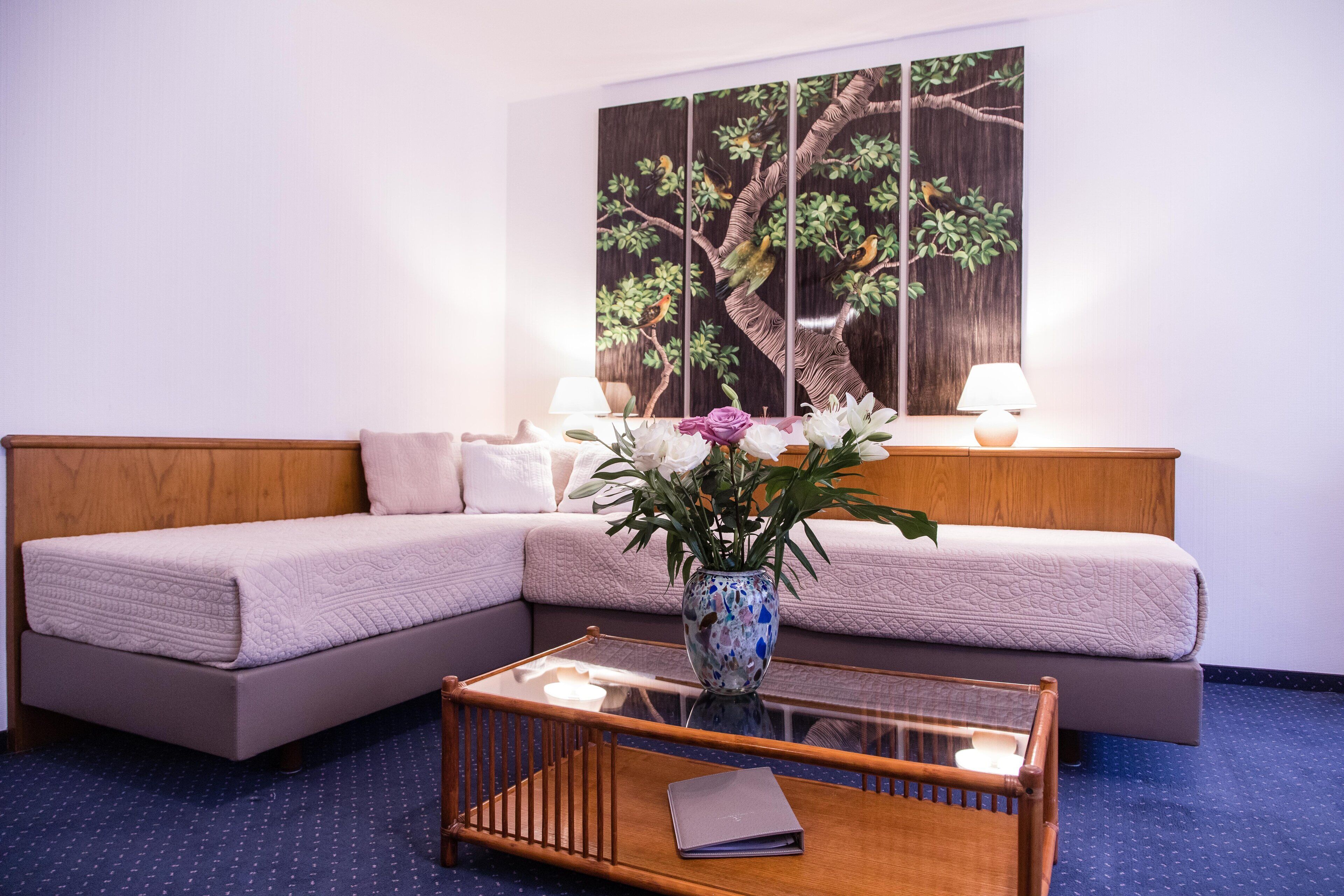 Una habitación de hotel moderna con sofá seccional, una mesa de centro de vidrio y un cuadro grande en la pared.