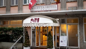 Exterior do Hotel Sagitta, com uma placa acima da entrada, uma árvore de Natal e uma rampa de acesso para cadeiras de rodas.
