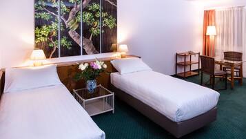 Habitació d'hotel amb dos llits individuals, un escriptori amb una cadira, una taula petita amb un ram de flors i un quadre gran a la paret.