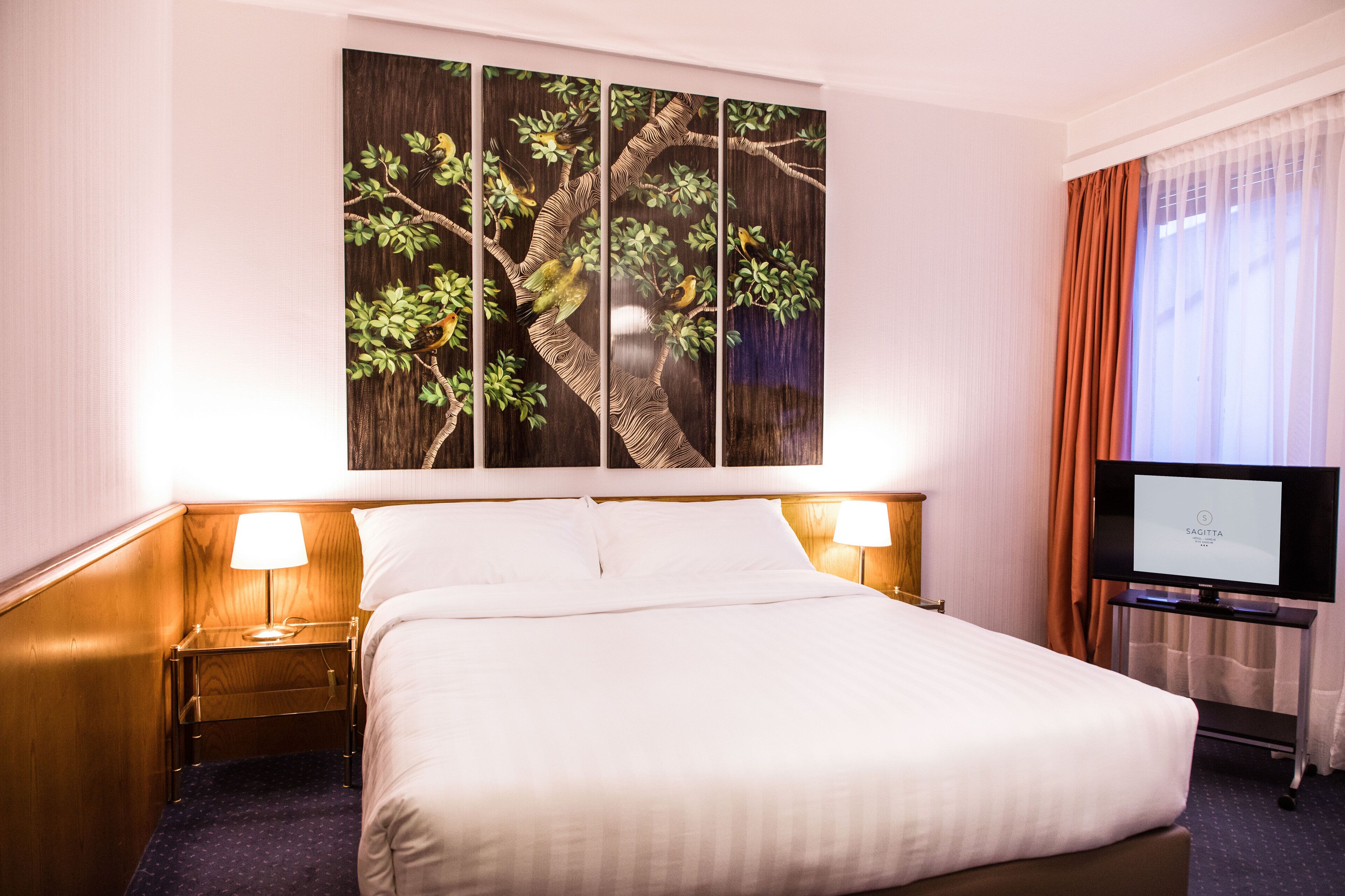 A hotel room with a large bed, two bedside lamps, a flat-screen TV, and a wall-mounted artwork depicting a tree.