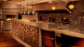 Una cocina moderna con protector contra salpicaduras de piedra, exhibición de troncos de madera e iluminación colgante.