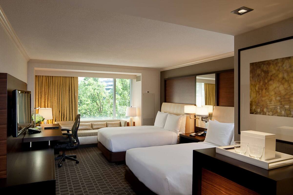 A hotel room with two beds, a desk, a chair, a TV, and a window with curtains.