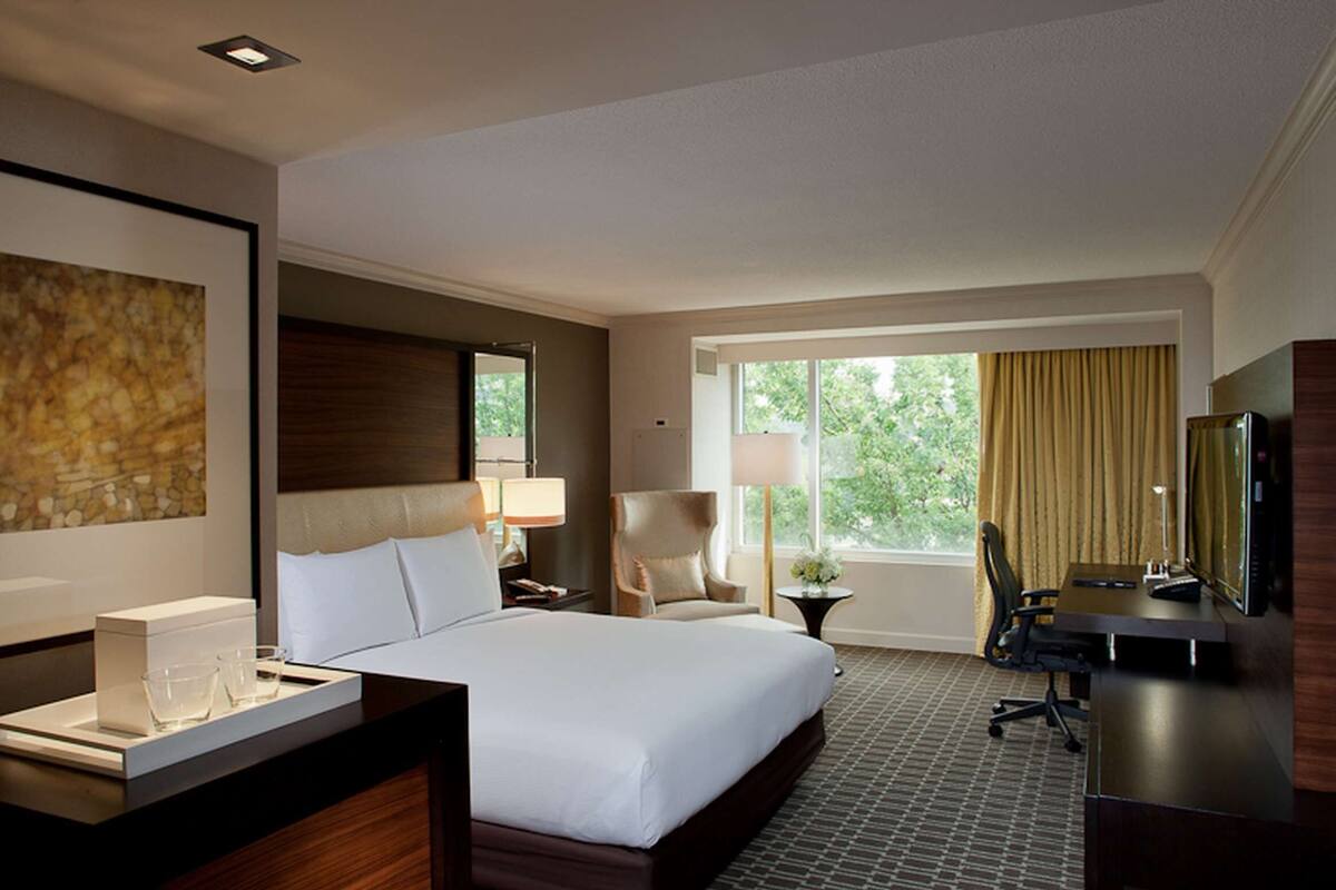 A hotel room with a large bed, a desk with a computer, a chair, a TV, and a window with curtains.