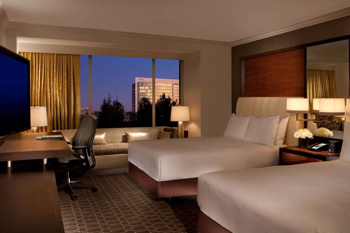 A hotel room with two beds, a desk, a chair, and a TV.
