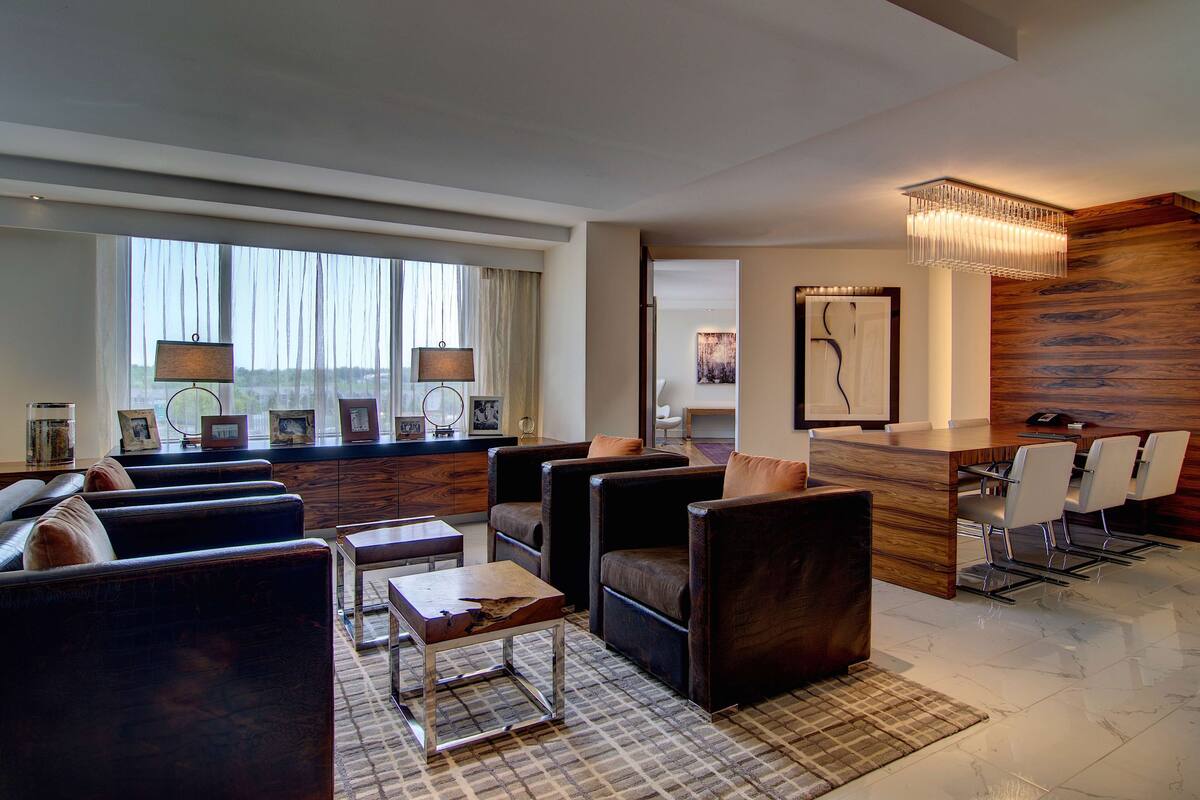 A modern living room with dark leather sofas, a wooden coffee table, and a dining area with a wooden table and chairs.