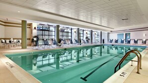 Una piscina interior con múltiples carriles, sillas de descanso y techo transparente.
