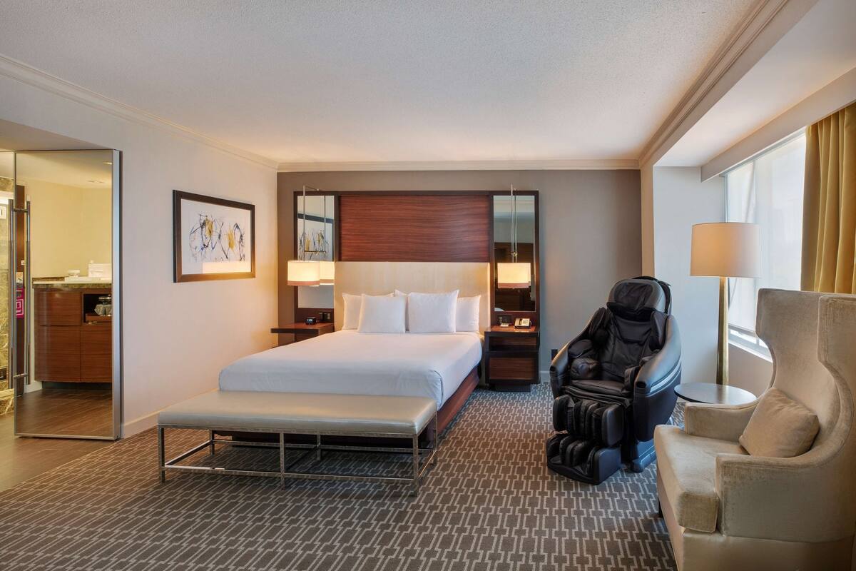 A hotel room with a large bed, a massage chair, a desk, and a chair.
