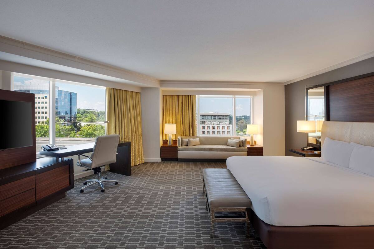 A hotel room with a large bed, a desk with a chair, a sofa, and a TV.