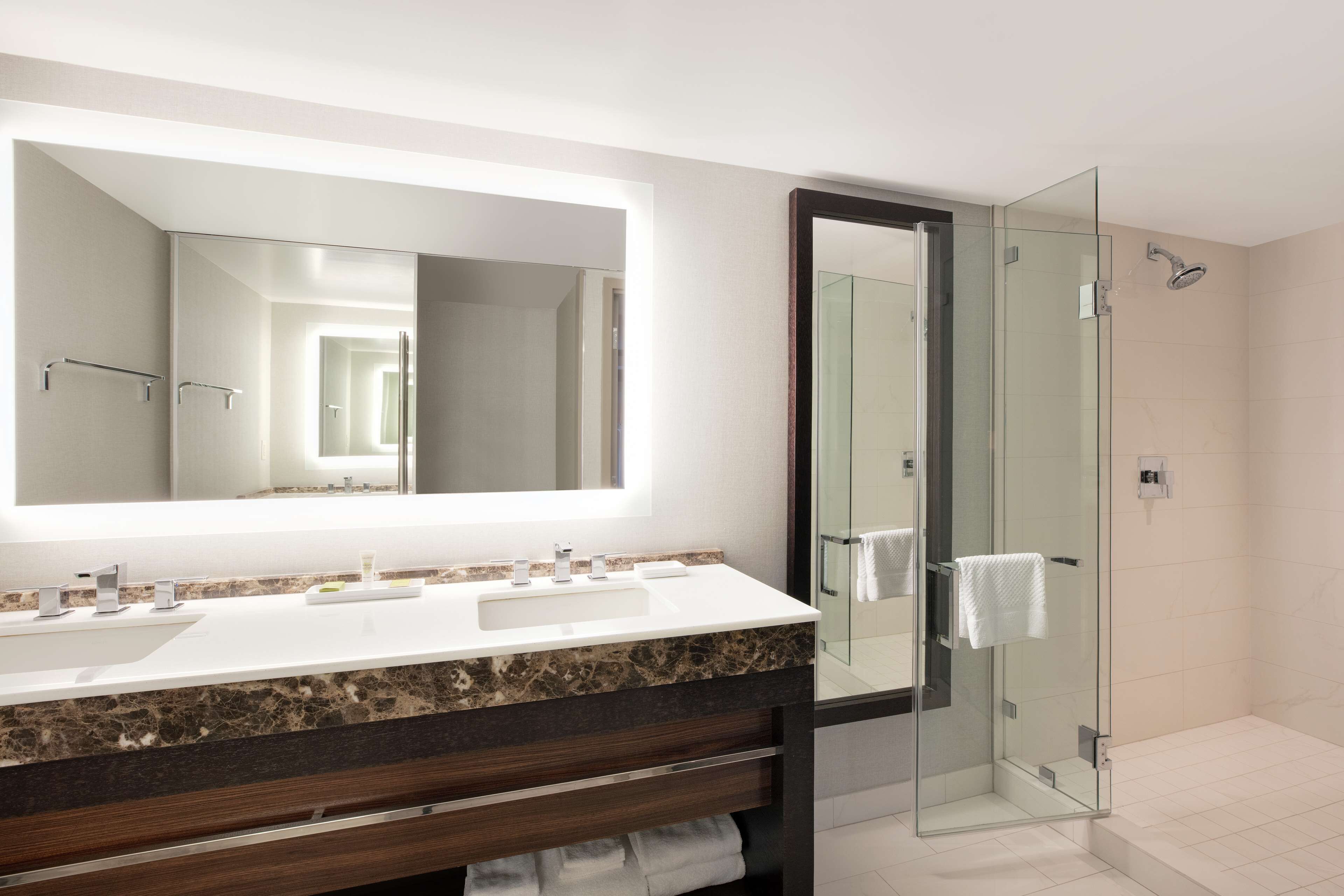 Un baño moderno con un espejo grande, lavamanos dobles y cabina de ducha con paredes de vidrio.
