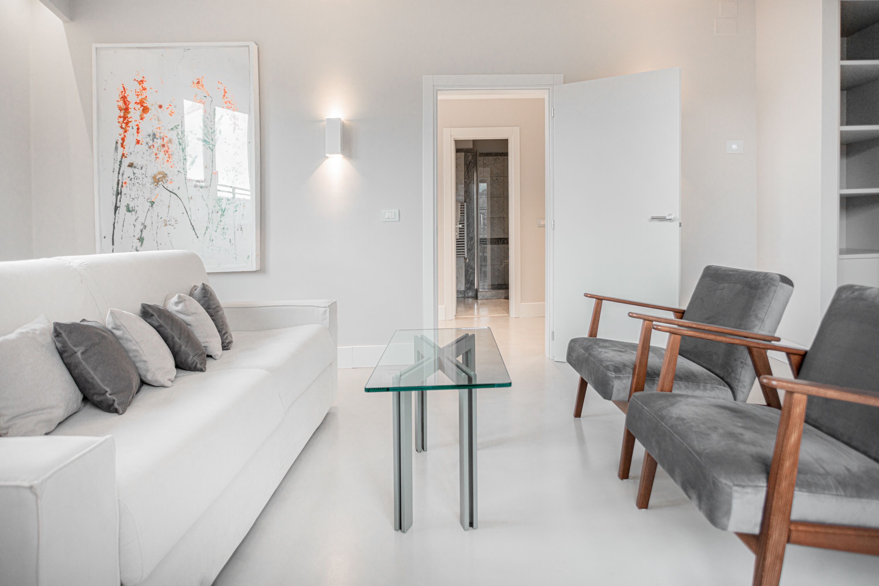 Una sala de estar moderna con una mesa de centro de vidrio, un sofá blanco y sillones grises.