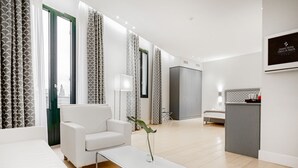 Quarto de hotel moderno com sofá branco, uma mesinha com uma planta, cama, escrivaninha e guarda-roupa.