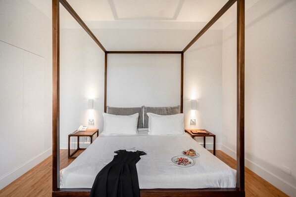 Un dormitorio moderno con cama con dosel, lámparas de noche y una cama bien hecha con una prenda negra y un plato de comida.