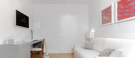 A modern, minimalist room with a white desk, chair, and sofa, a white door, and two framed abstract paintings.