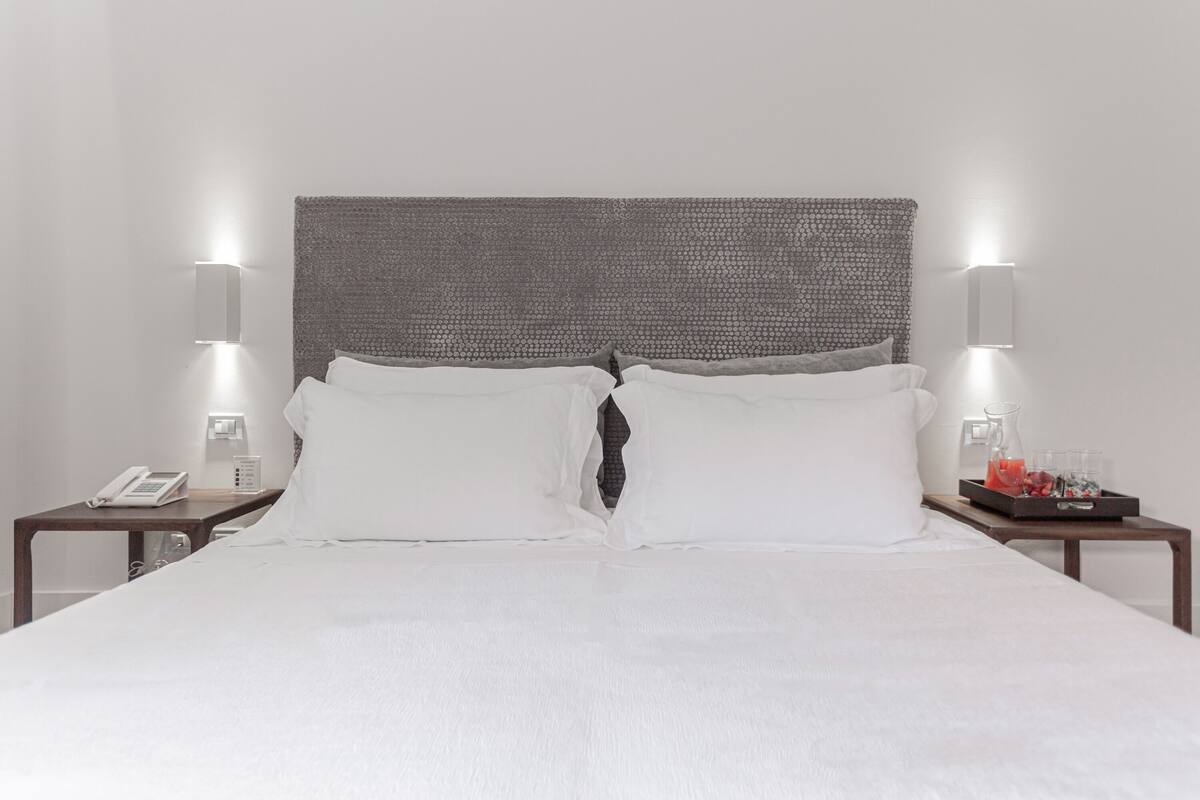 A neatly made bed with white linens, two bedside tables with lamps, and a tray with a glass of juice on one of the tables.