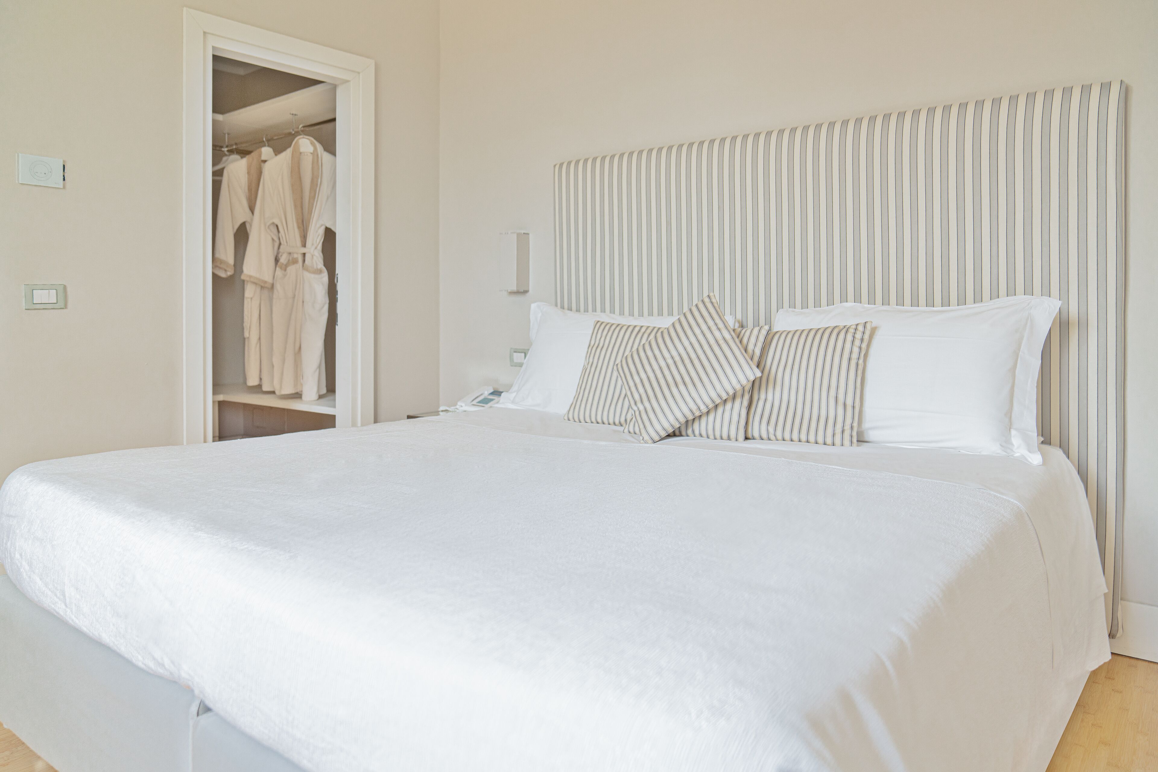 A neatly made bed with white bedding and striped pillows, a closet with hanging robes, and a striped headboard.