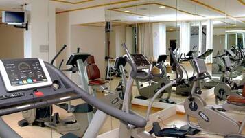 Una palestra con diverse macchine per esercizi, tra cui tapis roulant e cyclette, e un televisore montato a parete.