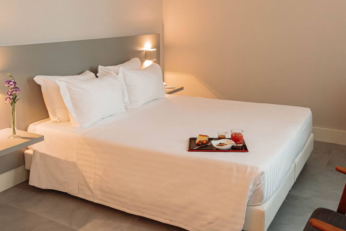 A neatly made bed with a tray of breakfast items, a vase of flowers, and a bedside table with a lamp.