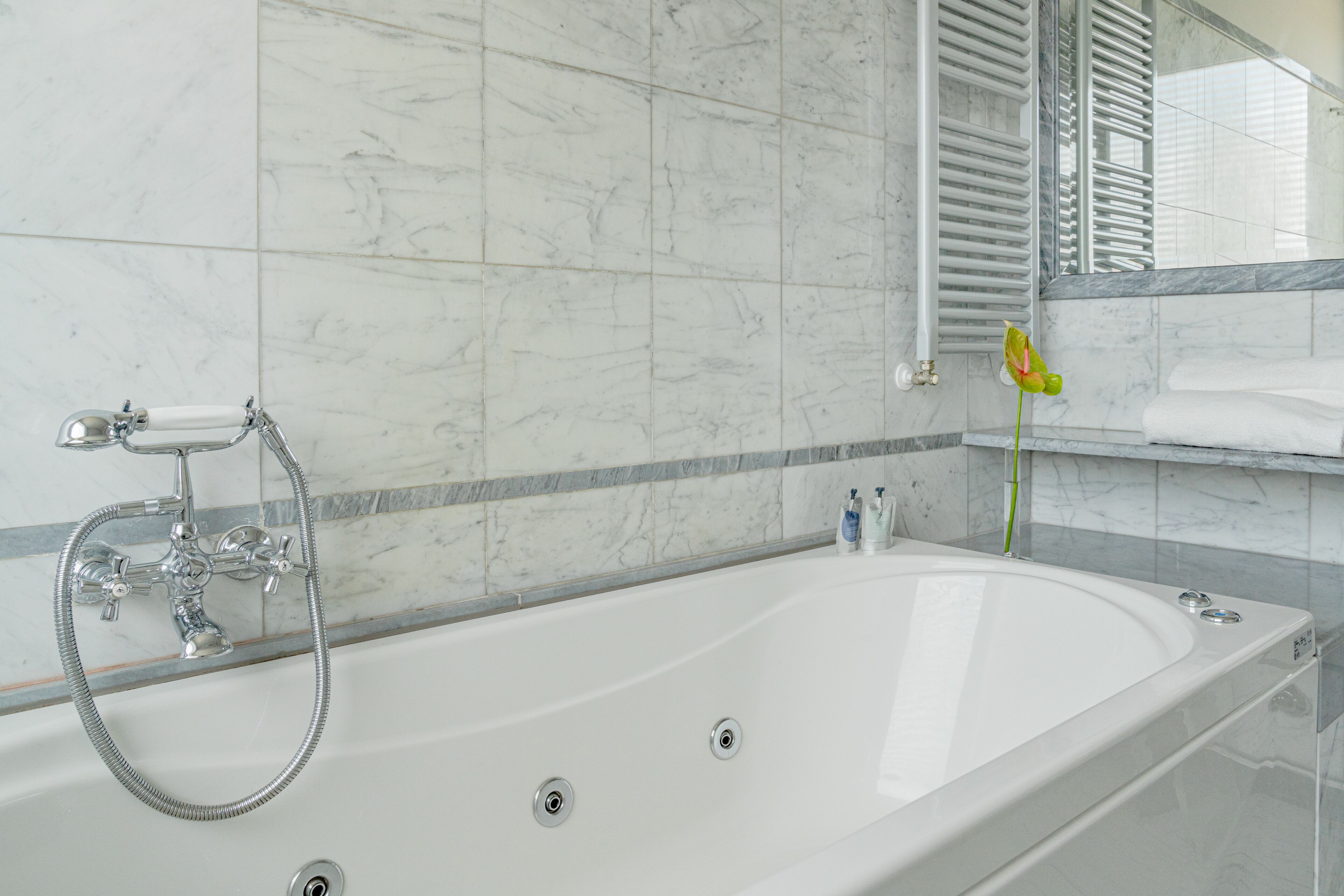 A modern bathroom with a large bathtub, a handheld showerhead, and a mirror above the sink.