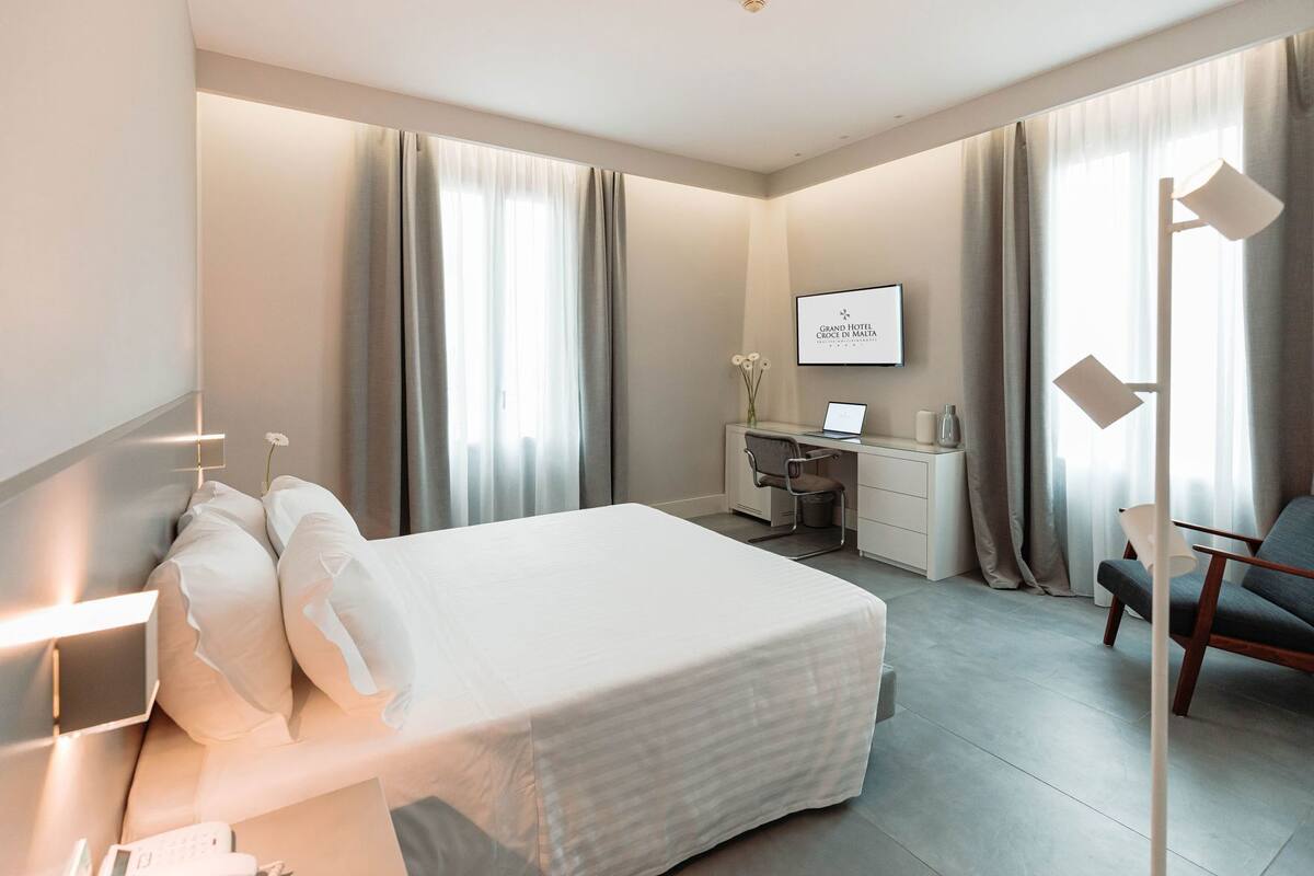 A hotel room with a bed, desk, chair, and a TV mounted on the wall.