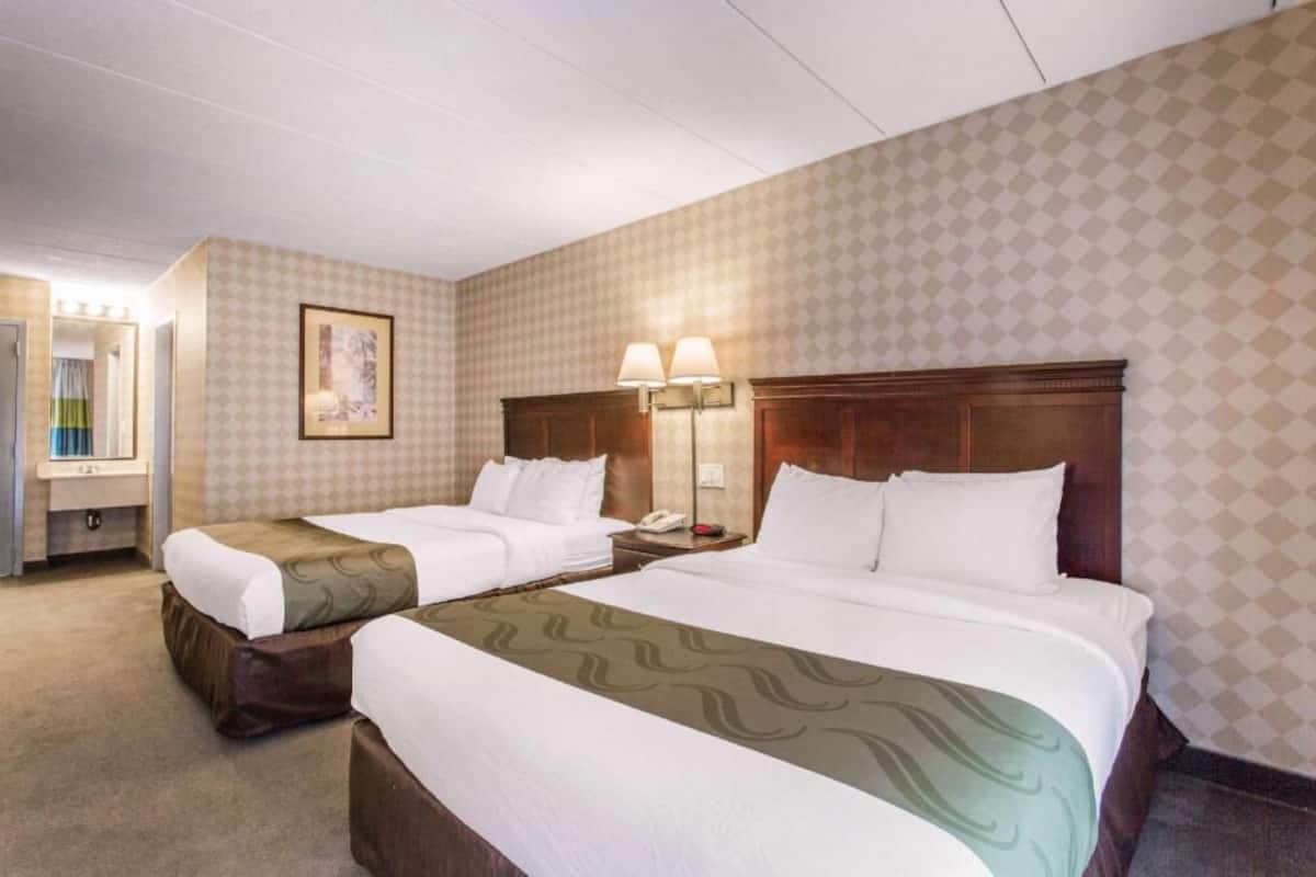 A hotel room with two beds, a nightstand with a lamp, a framed picture on the wall, and a bathroom with a mirror and sink.
