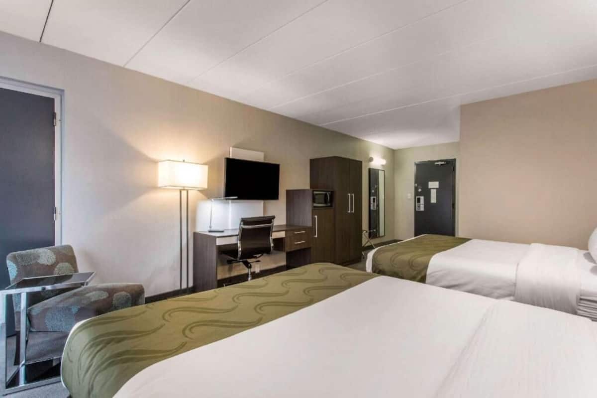 A hotel room with two beds, a desk, a chair, a TV, and a wardrobe.