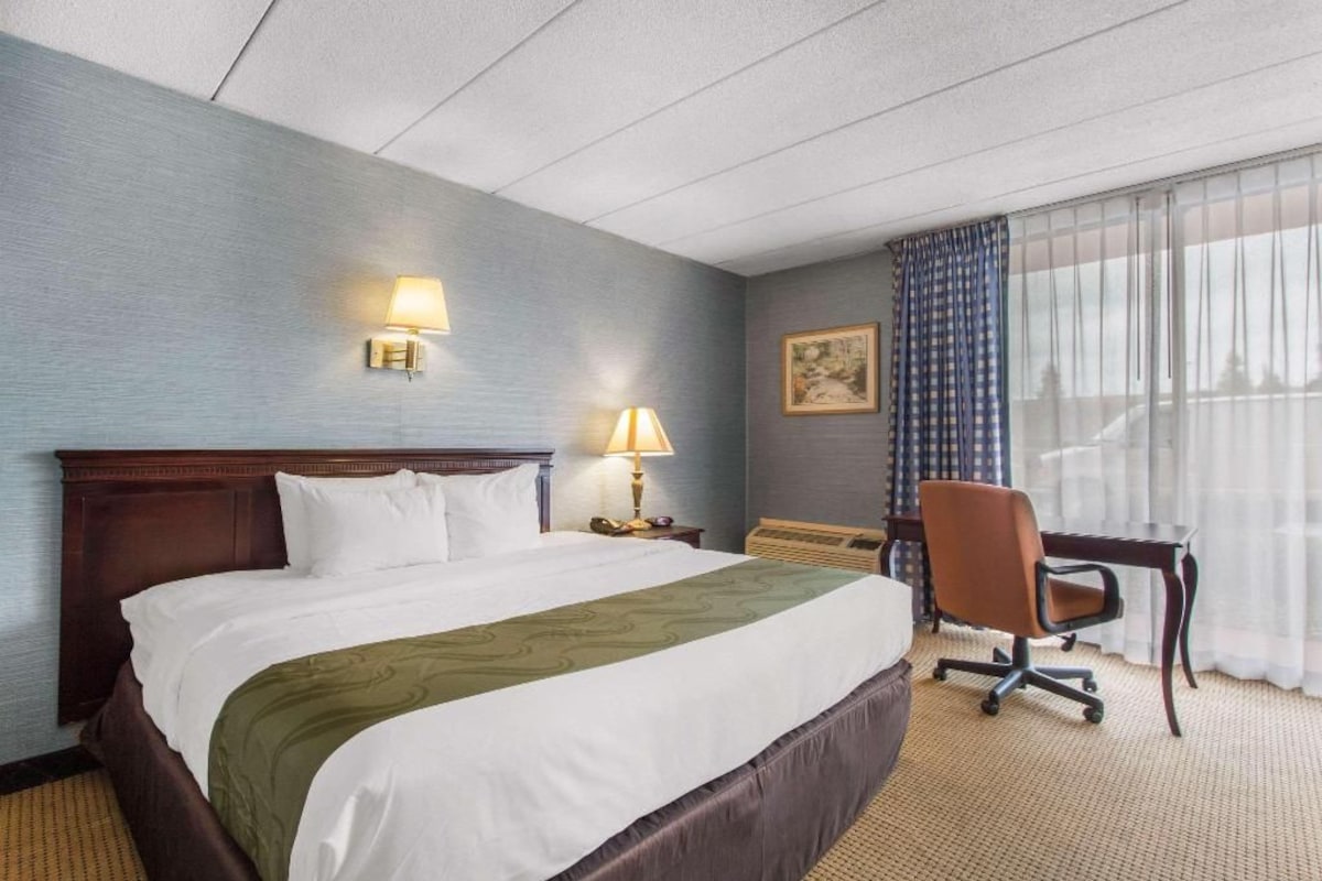 Habitación de hotel con una cama grande, dos lámparas de noche, un escritorio con una silla y una ventana con cortinas.