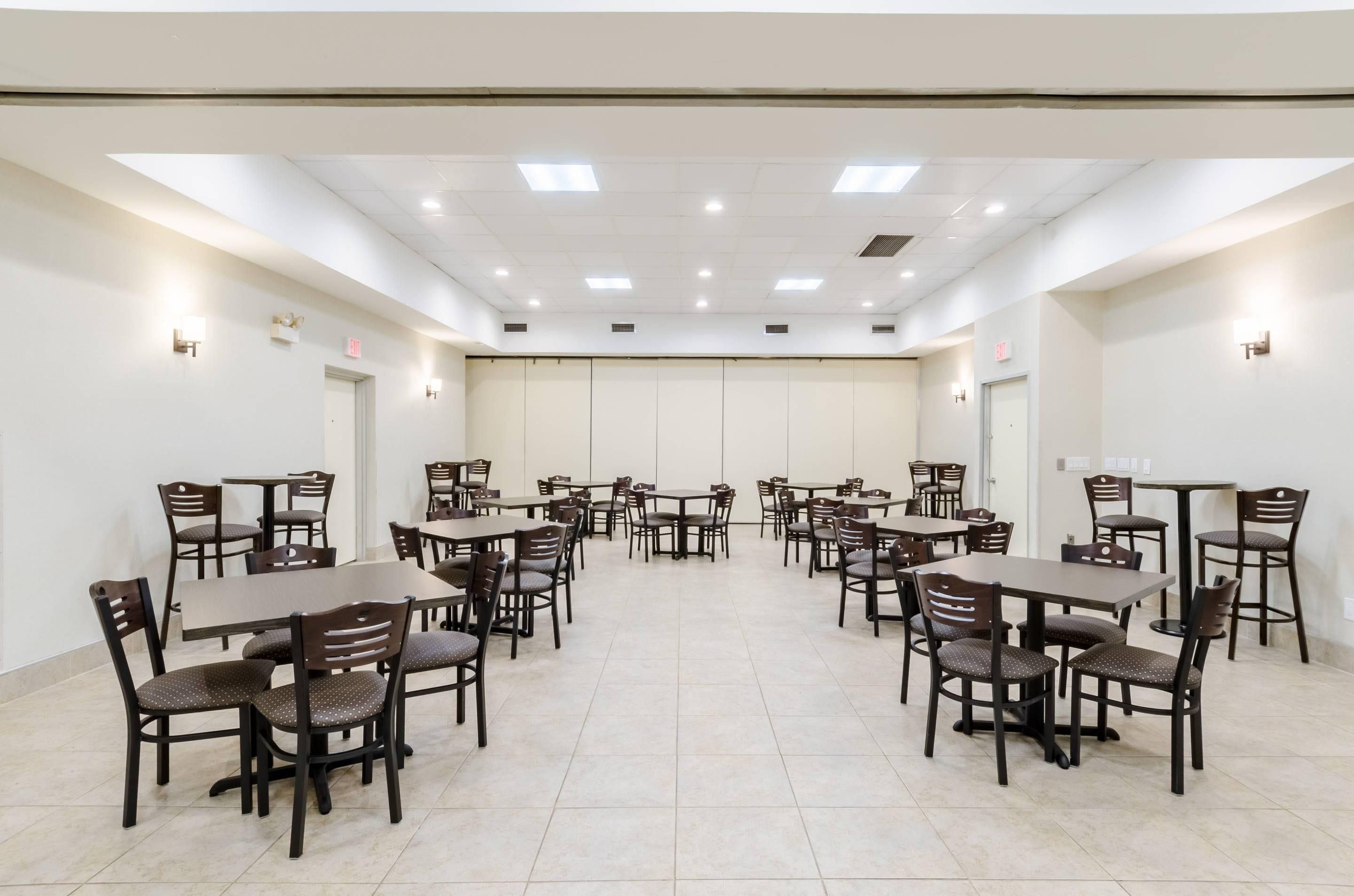 Une salle de conférence dotée de plusieurs tables et chaises, d’un éclairage encastré au plafond et de murs blancs.