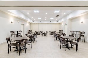 A conference room with multiple tables and chairs, recessed ceiling lights, and white walls.