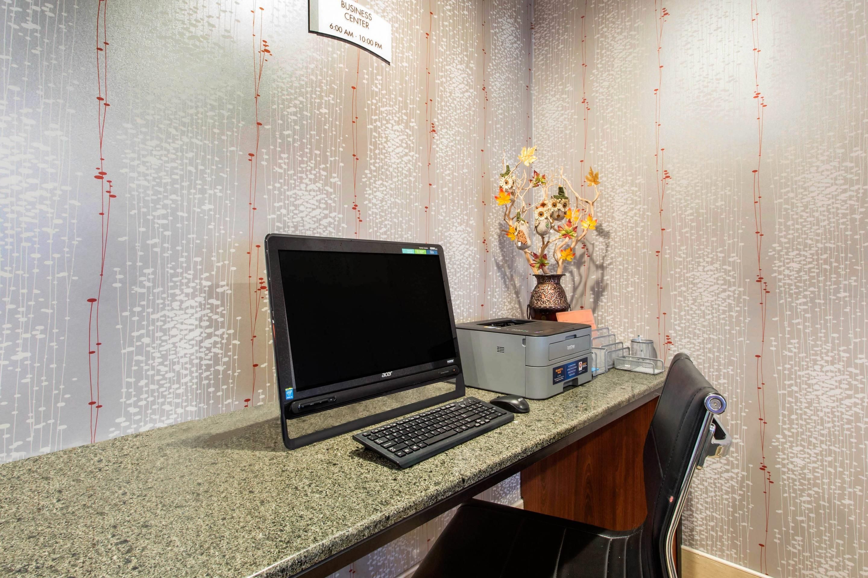A business center with a laptop, keyboard, and printer on a granite counter.