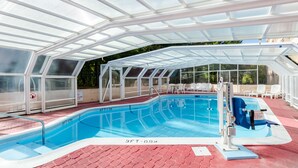 A covered swimming pool with glass walls, a diving board, and lounge chairs. - Quality Inn West Springfield (West Springfield)