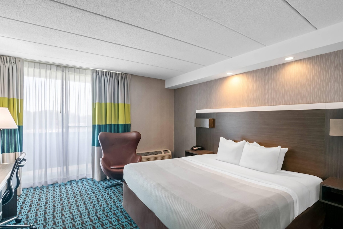 A hotel room with a bed, a chair, a desk, a lamp, and a window with curtains.