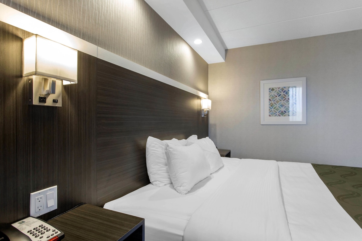 A hotel room with a neatly made bed, a bedside telephone, and wall-mounted lamps.