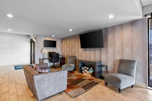 A modern living room with a sofa, two armchairs, a flat-screen TV, a fireplace, and a patterned rug.