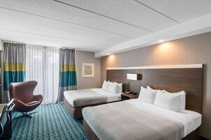 A hotel room with two beds, a desk, a chair, and a patterned carpet.