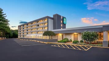 A multi-story hotel with a flat roof, a parking lot with marked spaces, and a sign indicating it is a Quality Inn.