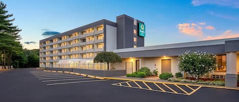 Um hotel com vários andares, teto plano, estacionamento demarcado e uma placa indicando ser um Quality Inn.