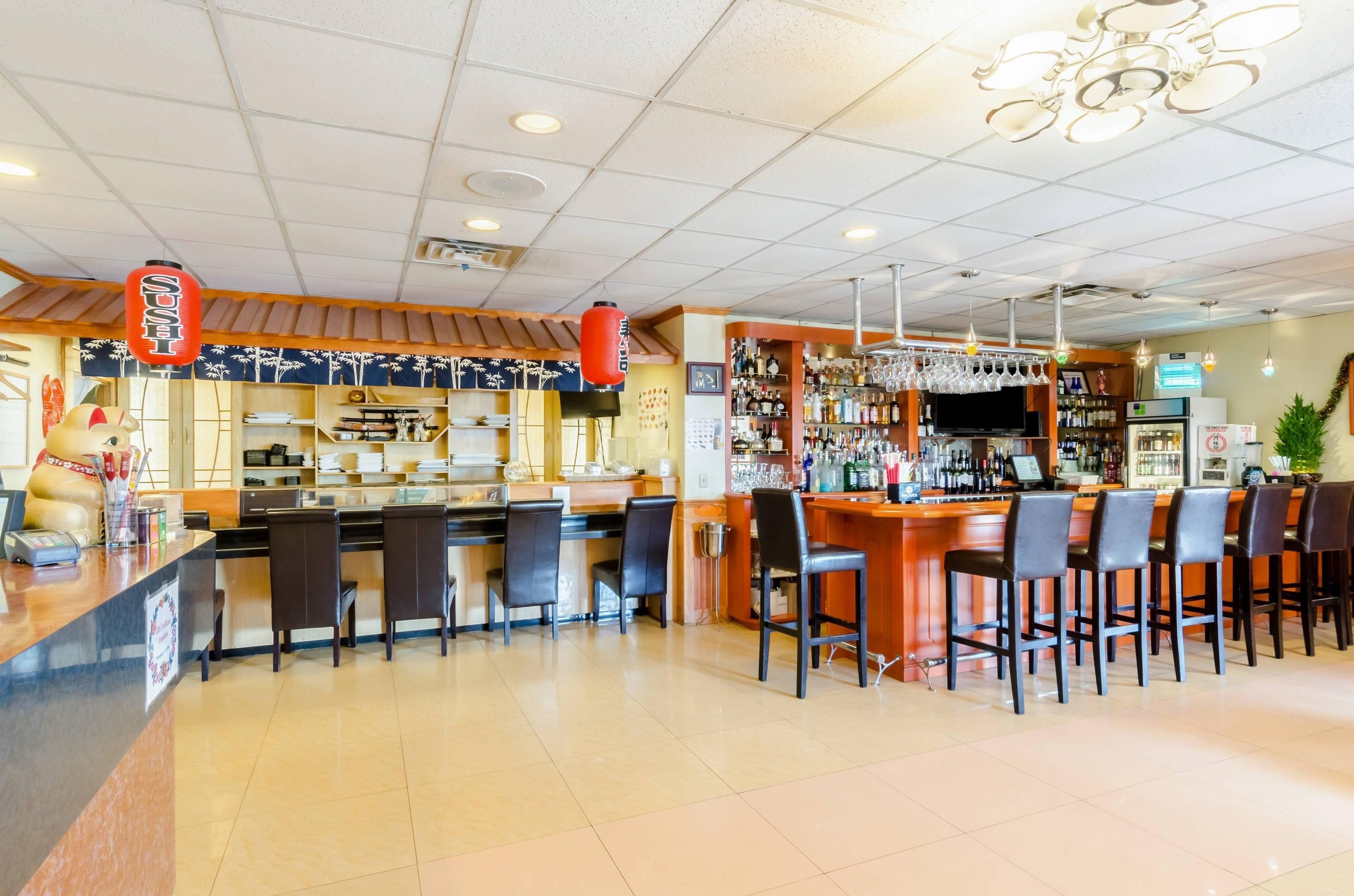 Eine Bar mit verschiedenen Sitzgelegenheiten, einer Theke mit Kasse und einer Auswahl an Flaschen und Gläsern auf Regalen.