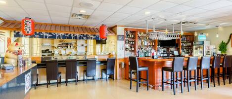Zona de bar con diversas opciones de asientos, una barra con caja registradora y una variedad de botellas y vasos en estanterías.