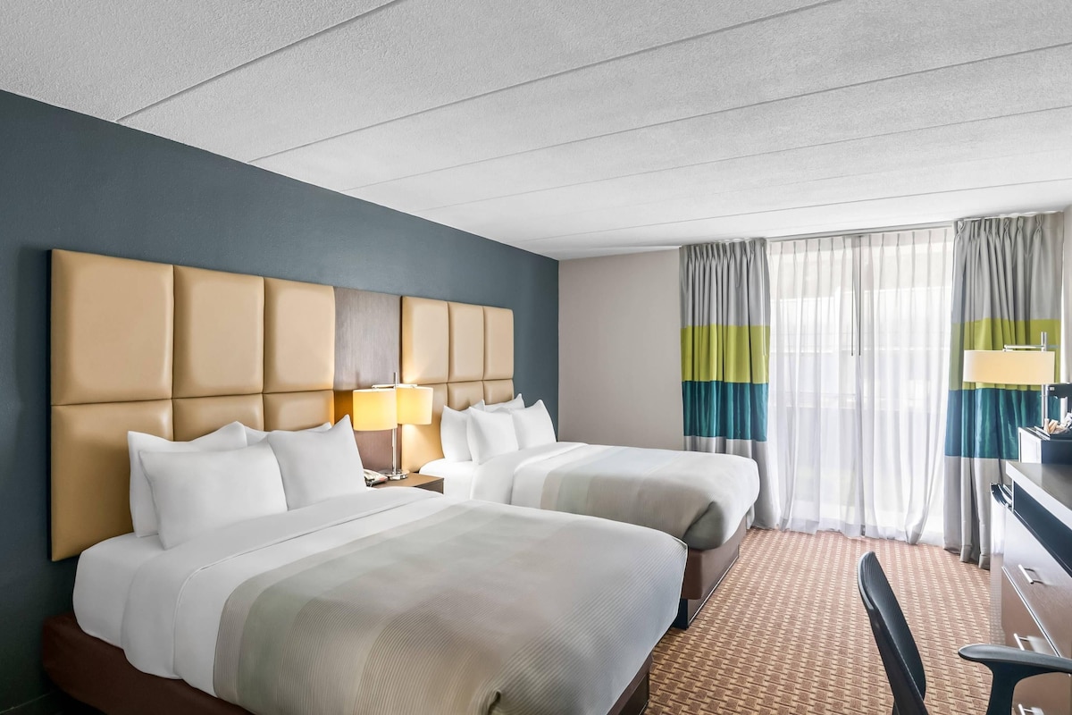 A hotel room with two beds, a desk, and a chair.