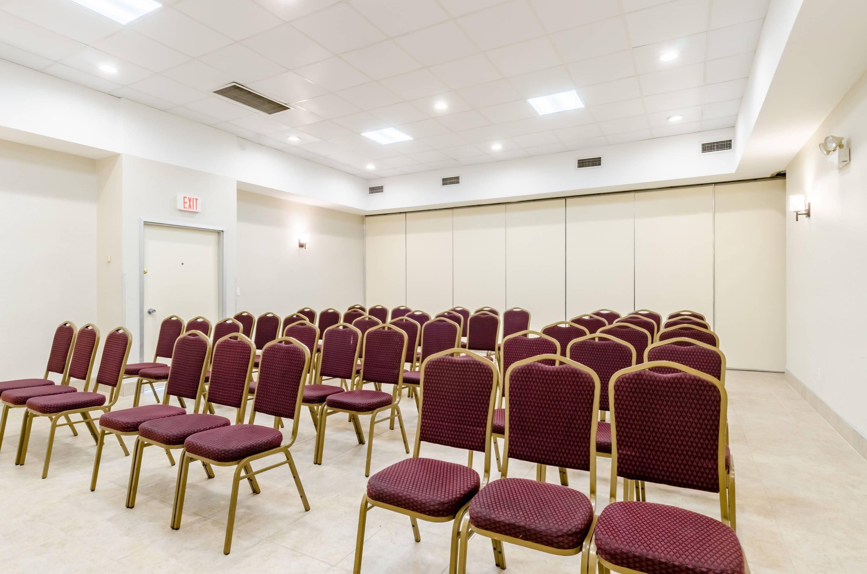 Une salle de conférence avec des rangées de chaises, un panneau indiquant la sortie et une porte.