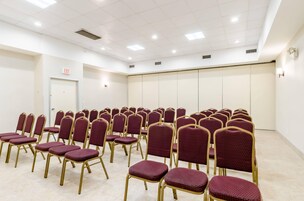 Un salón de conferencias con filas de sillas, un letrero de salida y una puerta.