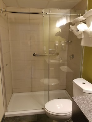 A shower with a glass door, a toilet, and a sink with a granite countertop. - Quality Inn West Springfield (West Springfield)