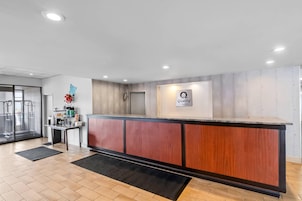 A hotel reception area with a wooden reception desk, a glass door entrance, and a sign indicating 'Quality by Choice Hotels'.