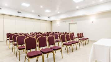 A conference room with rows of chairs and a white table, equipped with ceiling lights and an exit sign.