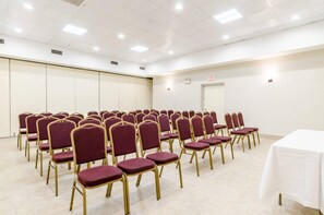 A conference room with rows of chairs and a white table, equipped with ceiling lights and an exit sign. - Quality Inn West Springfield (West Springfield)