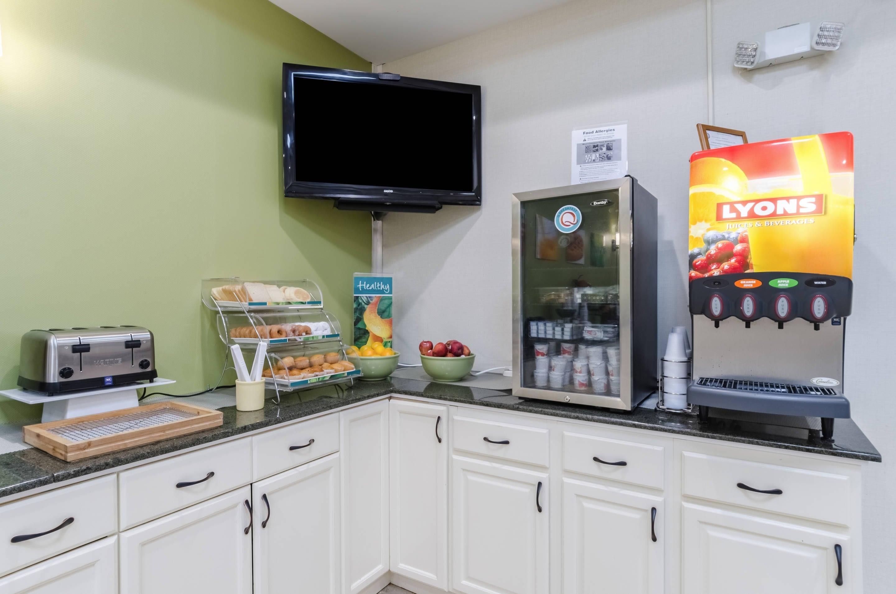 Un comedor con un tostador, un refrigerador, un dispensador de jugo y un televisor montado en la pared.