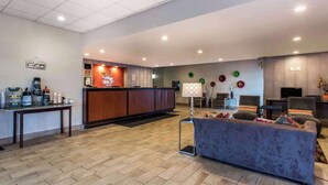 A spacious lobby with a reception desk, a coffee station, a seating area with a sofa and armchairs, and a television on a stand.