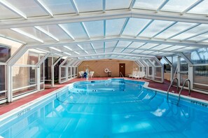 An indoor swimming pool with a glass ceiling, surrounded by lounge chairs and a wooden wall.